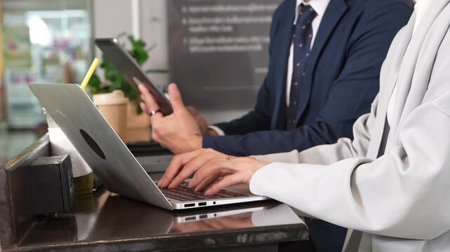 Hands of male and female employees typing on laptop keyboards in a coffee shop or coworking space.
