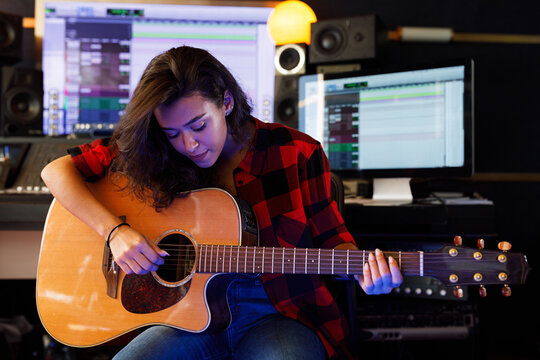 Woman playing on acoustic guitar in a recording studio