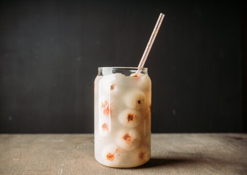 White lychee cocktail in a clear glass on dark background. Tropical drink with peeled lychee fruits.