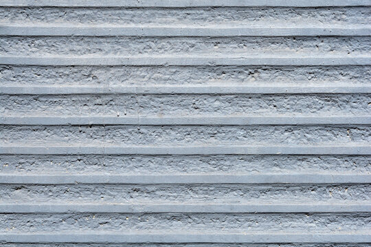 A close up background view of a grey concrete wall with a structured pattern of rough horizontal ridges and smooth parallel lines.