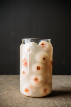 White lychee cocktail in a clear glass on dark background. Tropical drink with peeled lychee fruits.