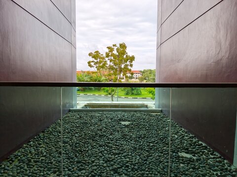 Modern architectural opening with pebble stone gravel terrace and glass railing framing green outdoor tree view