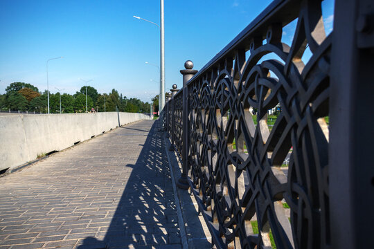 Close-up of decorative metal fence railings on paved pedestrian bridge under blue sky with copy space