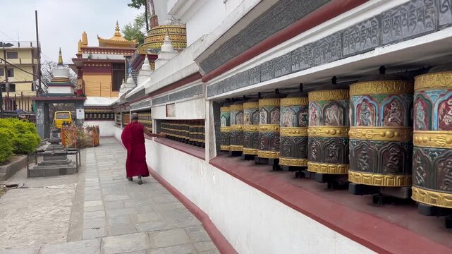 Buddhist monk in red robe spinning prayer wheels at Swayambhunath Complex in Kathmandu Nepal