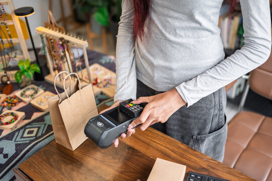 Woman accepting cashless payment with EDC terminal at small business retail store during customer purchase.