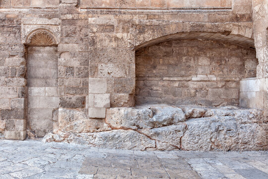 Architectural wall of calcarenite blocks featuring a recessed arch and sealed opening built over exposed carbonate rock substrate, showing stratigraphic integration and mixed masonry techniques.