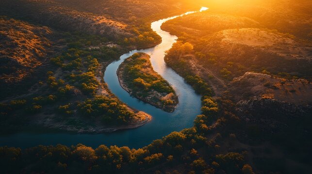 Aerial drone shot captures a winding river flowing through lush green valleys at golden hour with dramatic sunlight casting long shadows across the landscape. Ideal for environmental, ecological.