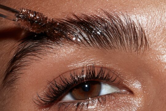 Closeup of person applying clear brow gel on eyebrow with a brush, creating a laminated look