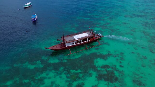 Traditional wooden boat with outriggers navigating clear turquoise waters at Turtle Beach. Concept of exclusive travel, vacation, and tropical adventure. Best aerial view pursuit drone flight