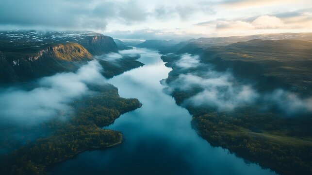 Aerial view of a serene river winding through misty mountains with soft clouds drifting over lush green valleys at dawn capturing natural beauty from above for travel and landscape inspiration.
