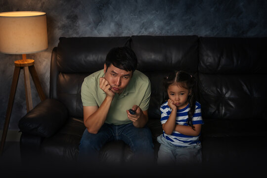 bored father and daughter watching tv in the living room at night