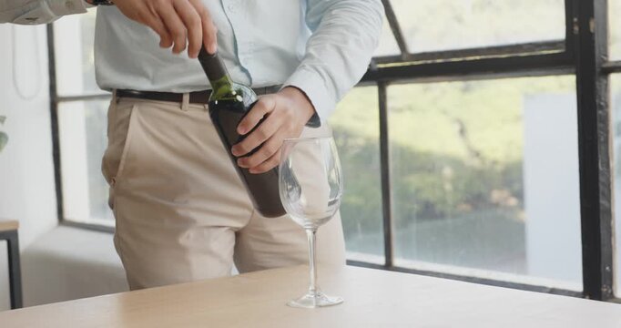 Person pouring red wine into glass by large window in bright office