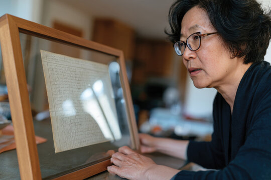 A woman examines a glass-framed historical manuscript, inviting curiosity about its stories and the tangible connection to past events etched in time.