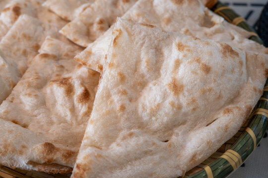 Fresh baked Indian naan flatbread slices served on a woven plate.