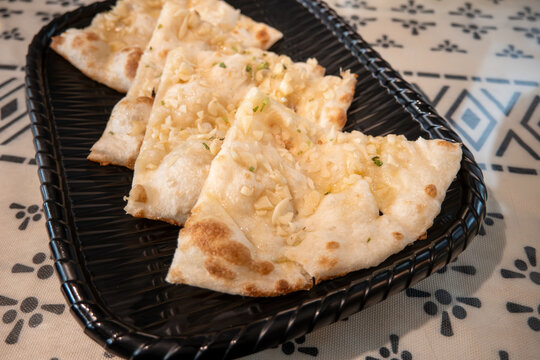 Fresh baked Indian naan flatbread slices served on a woven plate.