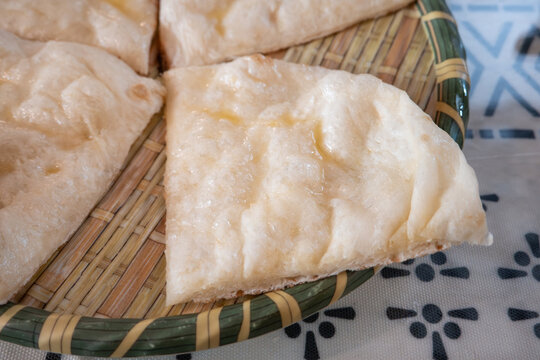 Fresh baked Indian naan flatbread slices served on a woven plate.