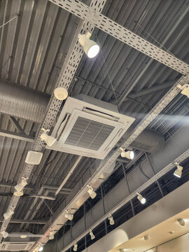 Modern infrastructure showing a functional hvac unit, metallic ventilation ducts, electrical cable trays, and bright spotlights on an exposed industrial ceiling. Vertical photo