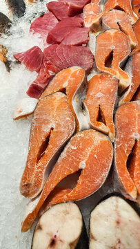 Slices of fresh red tuna fillets and vibrant orange salmon steaks displayed on a bed of crushed ice, highlighting healthy choices for seafood and cooking ingredients. Vertical photo