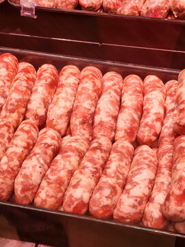 Raw fresh pork sausages are arranged in rows in a metal tray, ready for sale in a butcher shop display case, highlighting fresh meat products. Vertical photo