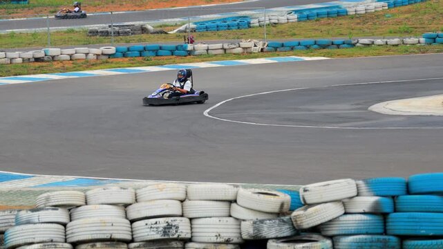 Go-kart racer driving on outdoor asphalt track with tire barriers