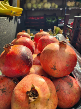 Pomegranates piled high for sale at an outdoor stall, showcasing fresh, ripe fruit available for purchase by customers looking for healthy, seasonal produce. Vertical photo