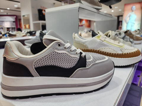 Sneakers and platform shoes are showcasing on a white shelf inside a modern retail footwear store, highlighting current fashion trends and consumer shopping experiences