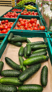 Cucumbers, tomatoes, and various fresh vegetables are abundant in crates on a supermarket produce aisle, offering healthy options for grocery shopping. Vertical photo