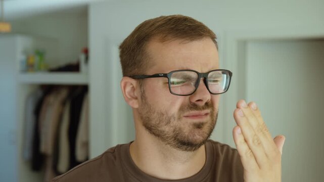 Man notices his own bad breath, reacts with discomfort and uses oral spray to freshen his breath.