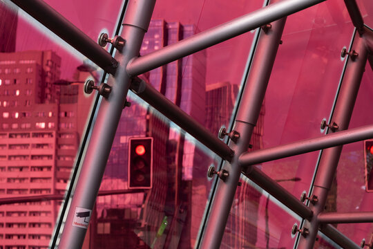 Red tinted urban scene seen through structural glass and metal framing with a traffic light and modern buildings creating an abstract city view
