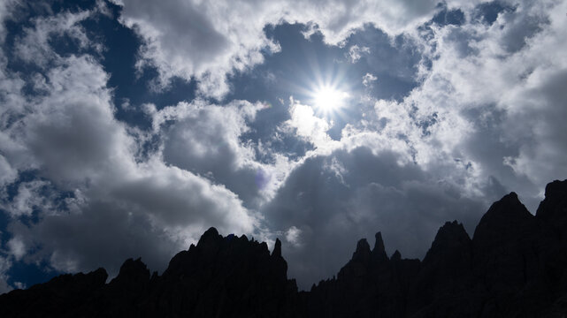 Die Sonne scheint durch eine Wolkenl&uuml;cke &uuml;ber Bergspitzen in den Dolomiten