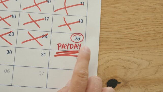 Close-up of a finger pointing at a payday date marked on a calendar after previous days were crossed off, representing salary payment and financial anticipation.