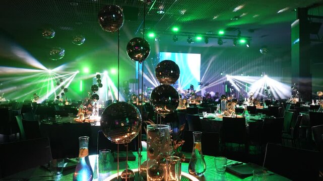 Elegant event setup featuring illuminated tables with decorative glass spheres and vibrant lighting, creating a festive atmosphere in a modern banquet hall
