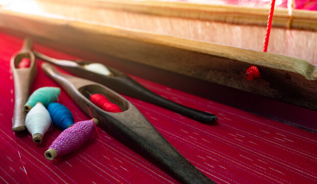 Traditional wooden weaving shuttle and colorful thread on red handmade fabric, textile loom tools used by artisan for cloth production, cultural craftsmanship and heritage weaving technique.