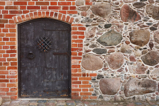 Weathered wooden door framed by red brick and rough stone wall