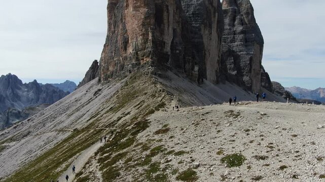 Hikers on a rocky trail below the massive rock peaks of Tre Cime di Lavaredo in the Italian Dolomites in Tre Cime di Lavaredo, Dolomites, Italy