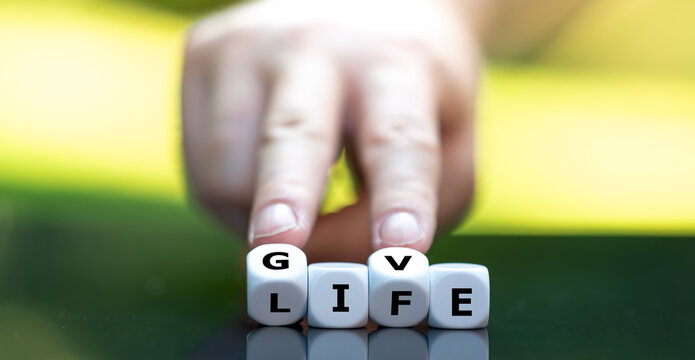 Human fingers turn letter cubes from LIFE to GIVE, symbolising generosity, charity, organ donation, blood donation and the gift of life.