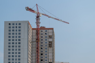 Construction workers elevate a new structure with a crane under a clear blue sky © beholdereye