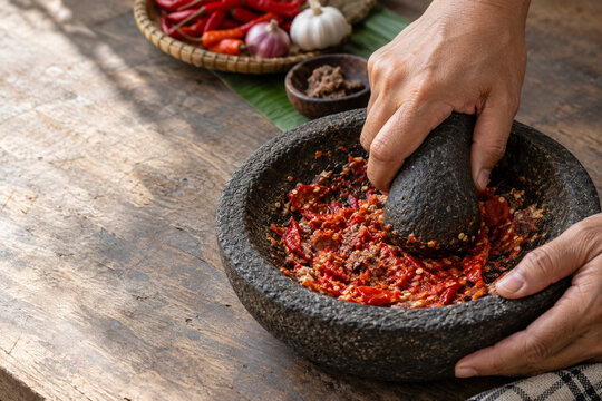 Hands Grinding Red Chilies and Terasi in Traditional Stone Mortar