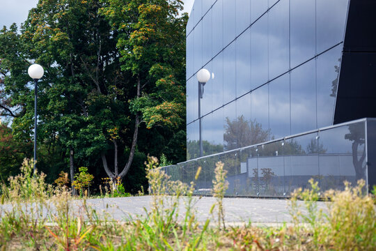 Modern office building with glossy black glass facade reflects cloudy sky and green park trees with copy space