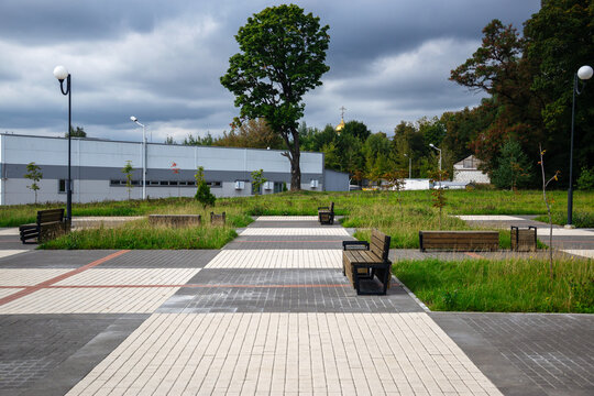 Empty wooden benches stand on patterned paved tiles of quiet public park lane under dramatic stormy sky with copy space