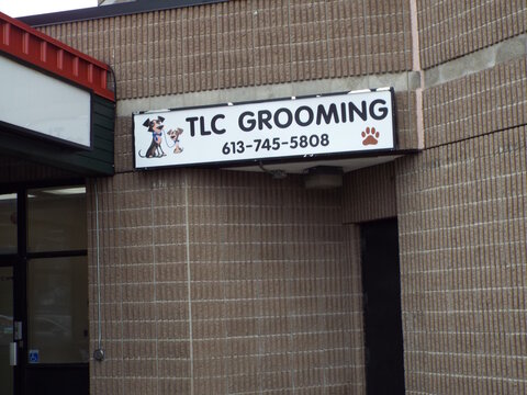  Gloucester, Ontario, Canada &ndash; July 12, 2026: An outdoor view showing the storefront exterior and corporate sign for "TLC Grooming" mounted on a brick wall at 5303 Canotek Rd Unit 20A.