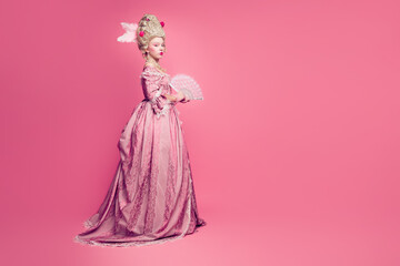 Fototapeta premium Photo of gorgeous wealthy lady in baroque style antique dress enjoying ballroom occasion holding fan isolated pink color background
