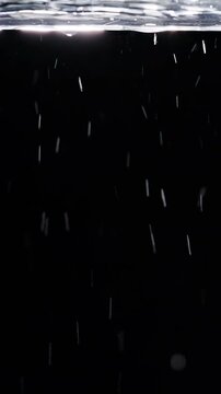 Vertical video. Water Droplets Fall Beneath a Rippling Surface Against Black Background, Creating a Clean Abstract View of Freshness and Fluid Motion