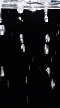 Vertical video. Melting Ice Releases Clear Water Droplets Against a Deep Black Background, Showing Cold Weather and Natural Thawing