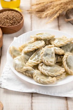Boiled vareniki dumplings stuffed with bryndza cheese and green herbs served on white plate on rustic table