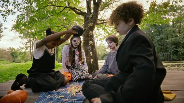 Diverse teenagers in Halloween costumes pouring candies and giving high fives outdoors in slow motion. Clip suitable for youth holiday advertising and autumn seasonal marketing