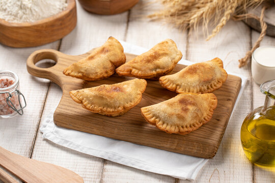 Crispy golden fried mini chebureki meat turnovers served on wooden cutting board with rustic ingredients