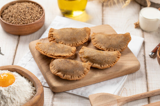 Crispy golden fried mini chebureki meat turnovers served on wooden cutting board with rustic ingredients