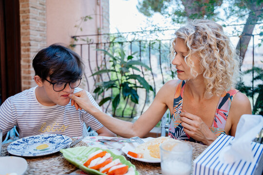 Single mother gently helping teenage son with Down syndrome during breakfast at home in Spain