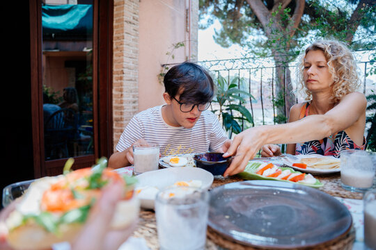 Single mother and two sons sharing quiet breakfast surrounded by plants on home terrace in Spain